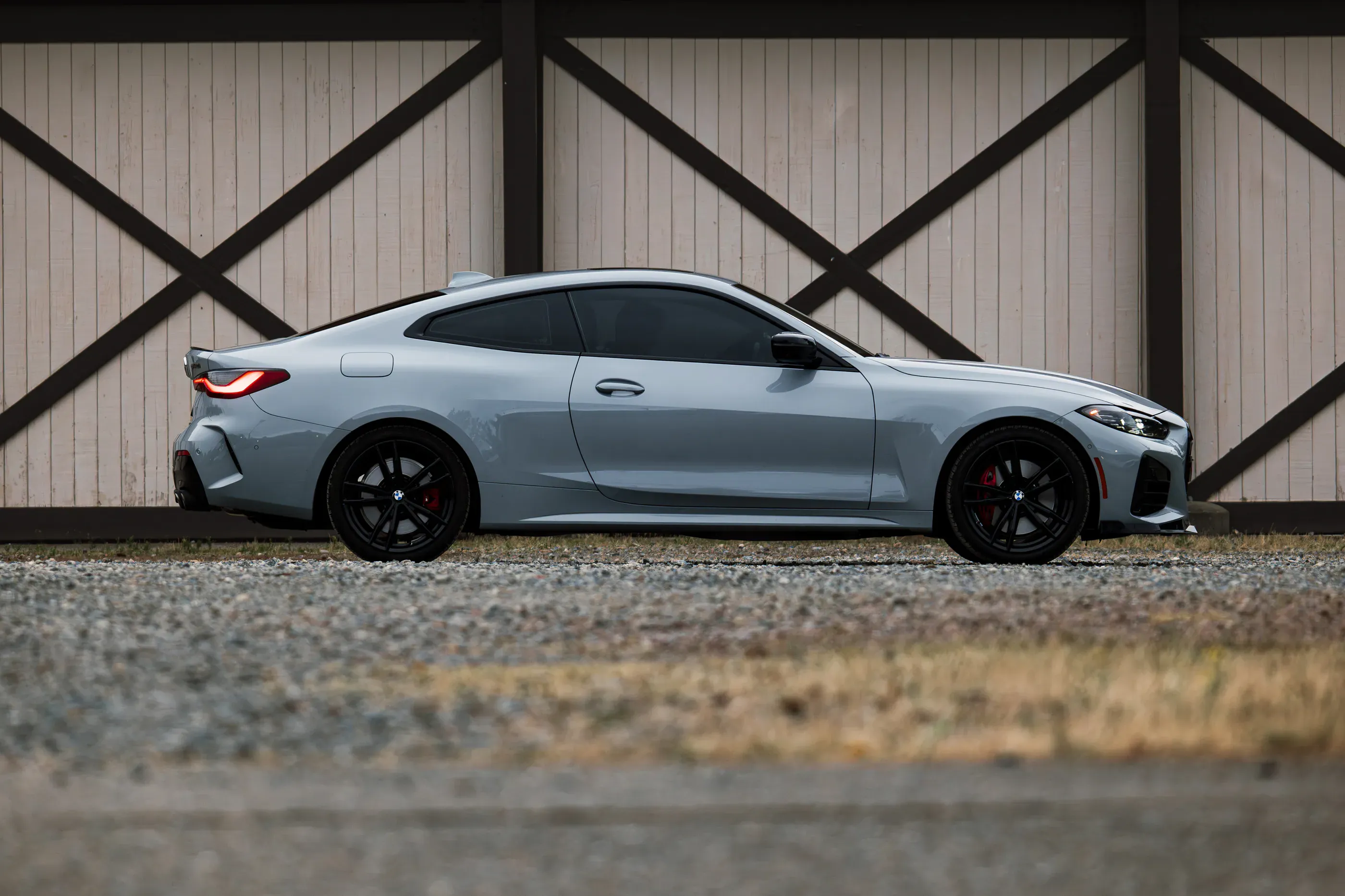 Side profile of a grey BMW M440i coupe parked in front of a barn-style building.