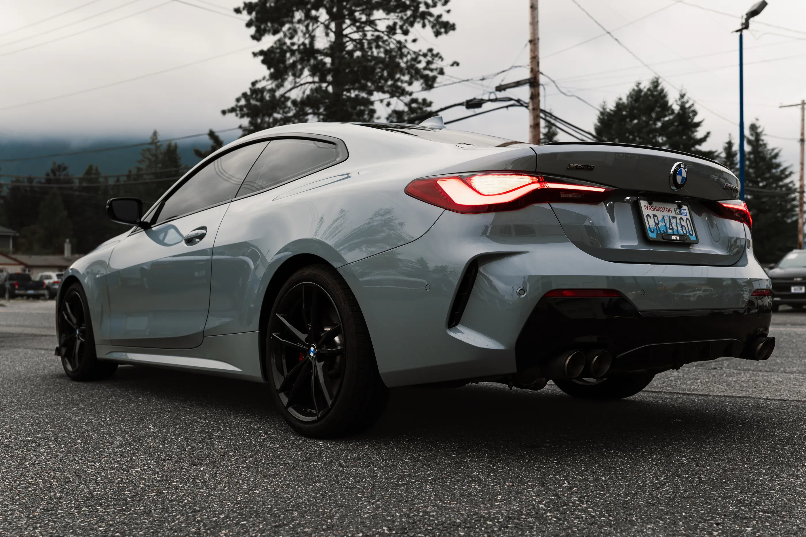 Rear three-quarter view of a grey BMW M440i coupe on a wet road at dusk.