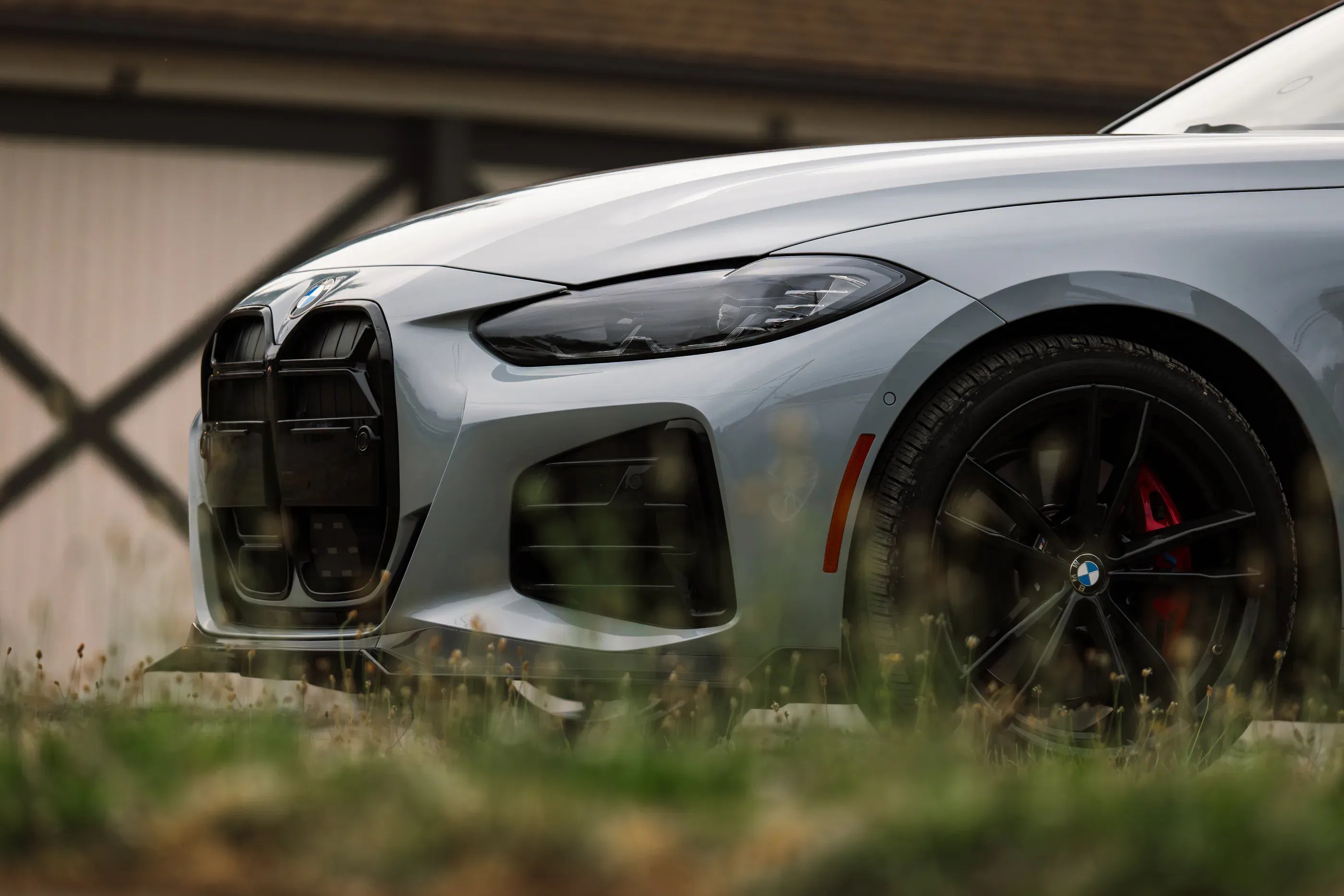 Close-up of the grille and headlight of a grey BMW M440i photographed through tall grass.
