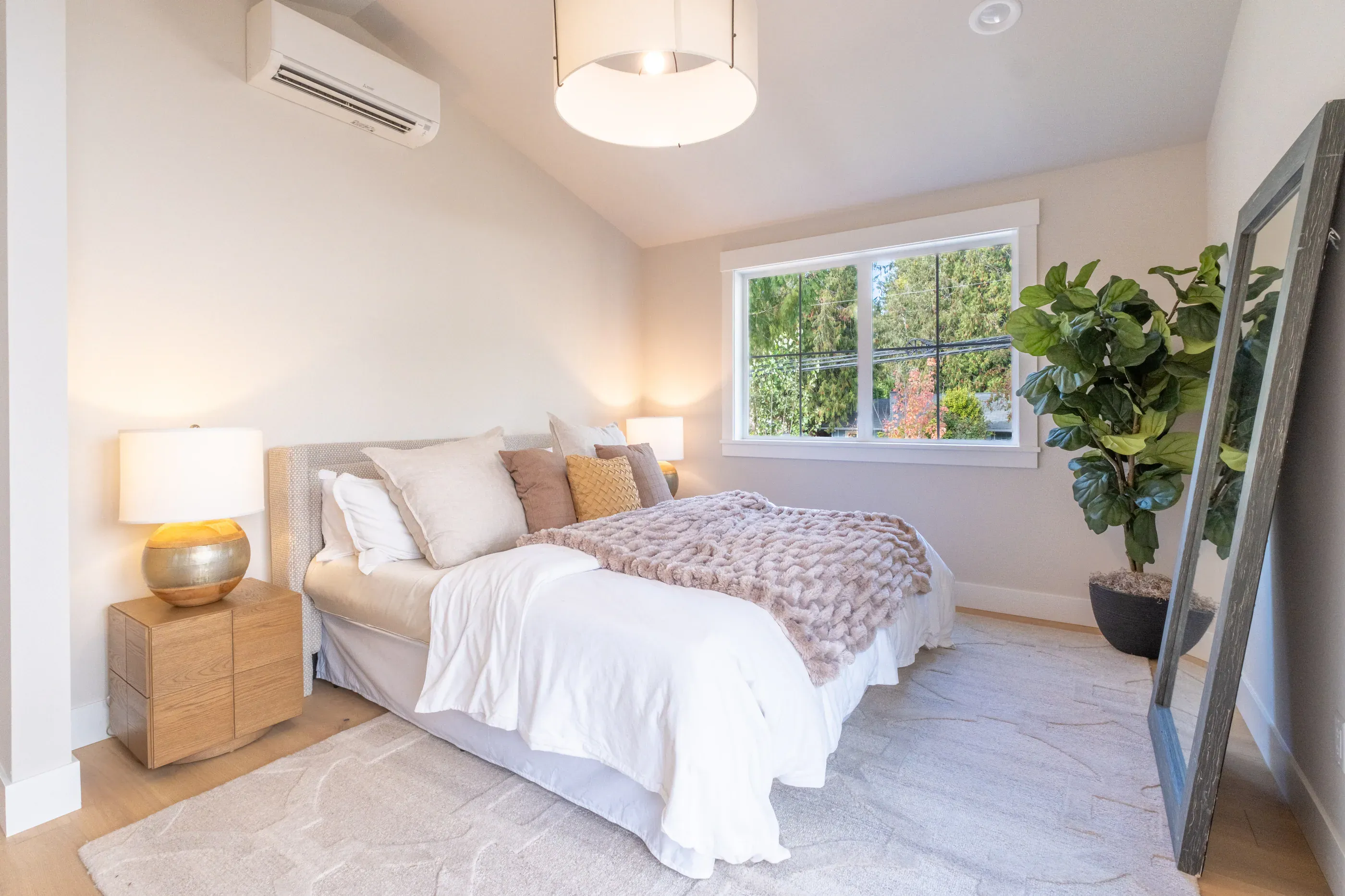 Bright bedroom with plant, lamp, and white bedding.