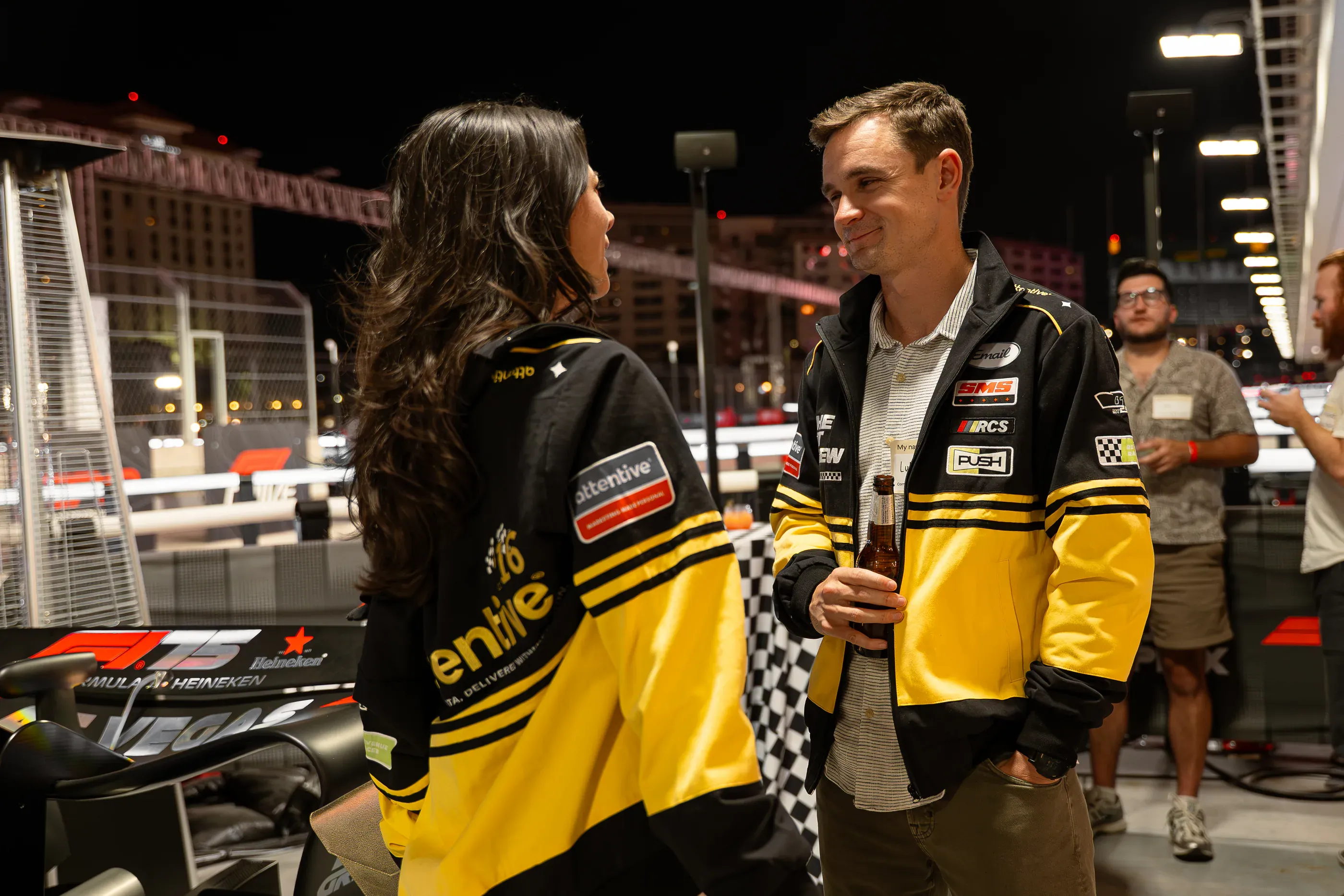 Two staff members stand near Attentive-branded vehicles at night.