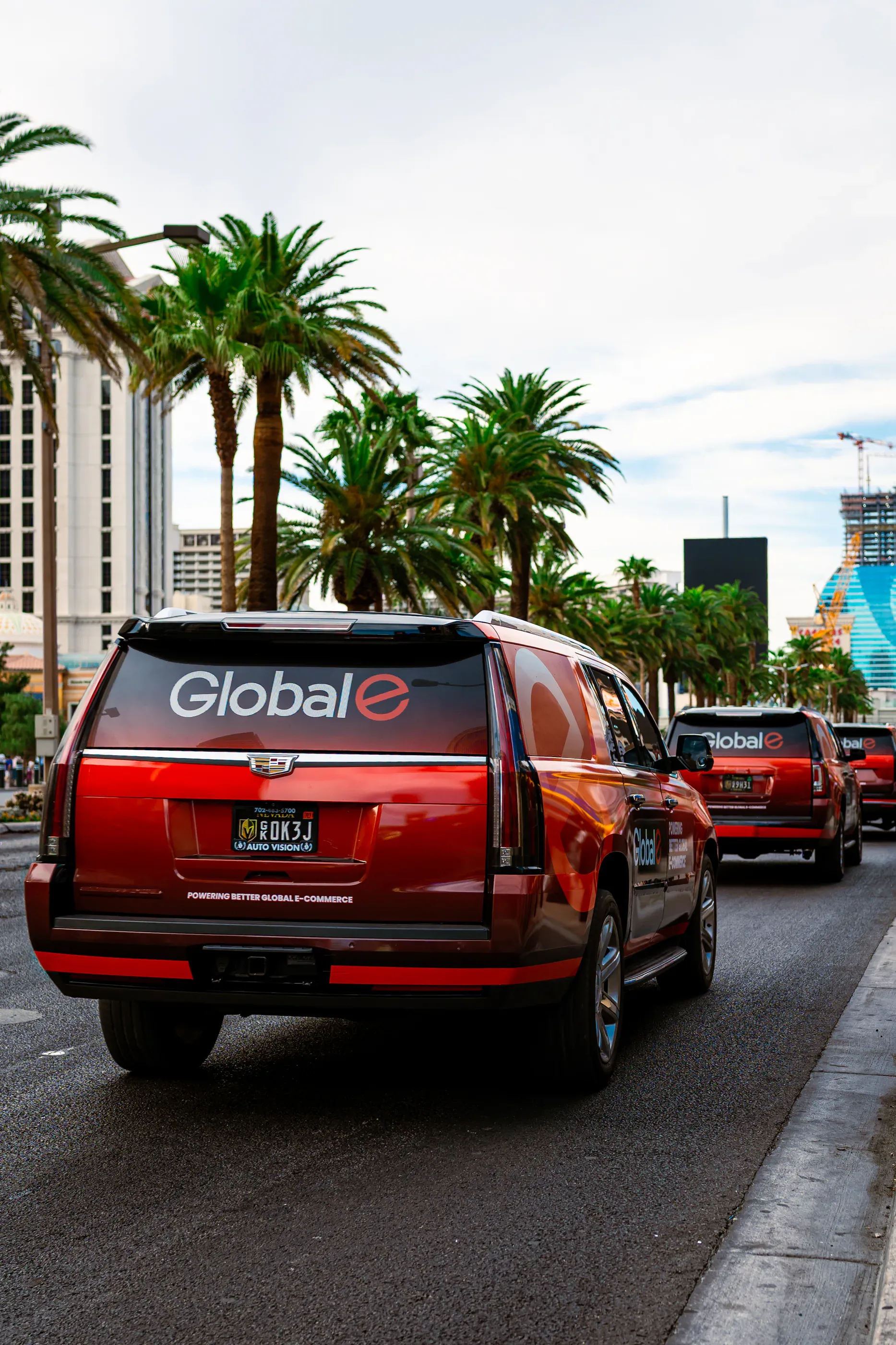 Red Globale-branded vehicle moves through traffic near palm trees.