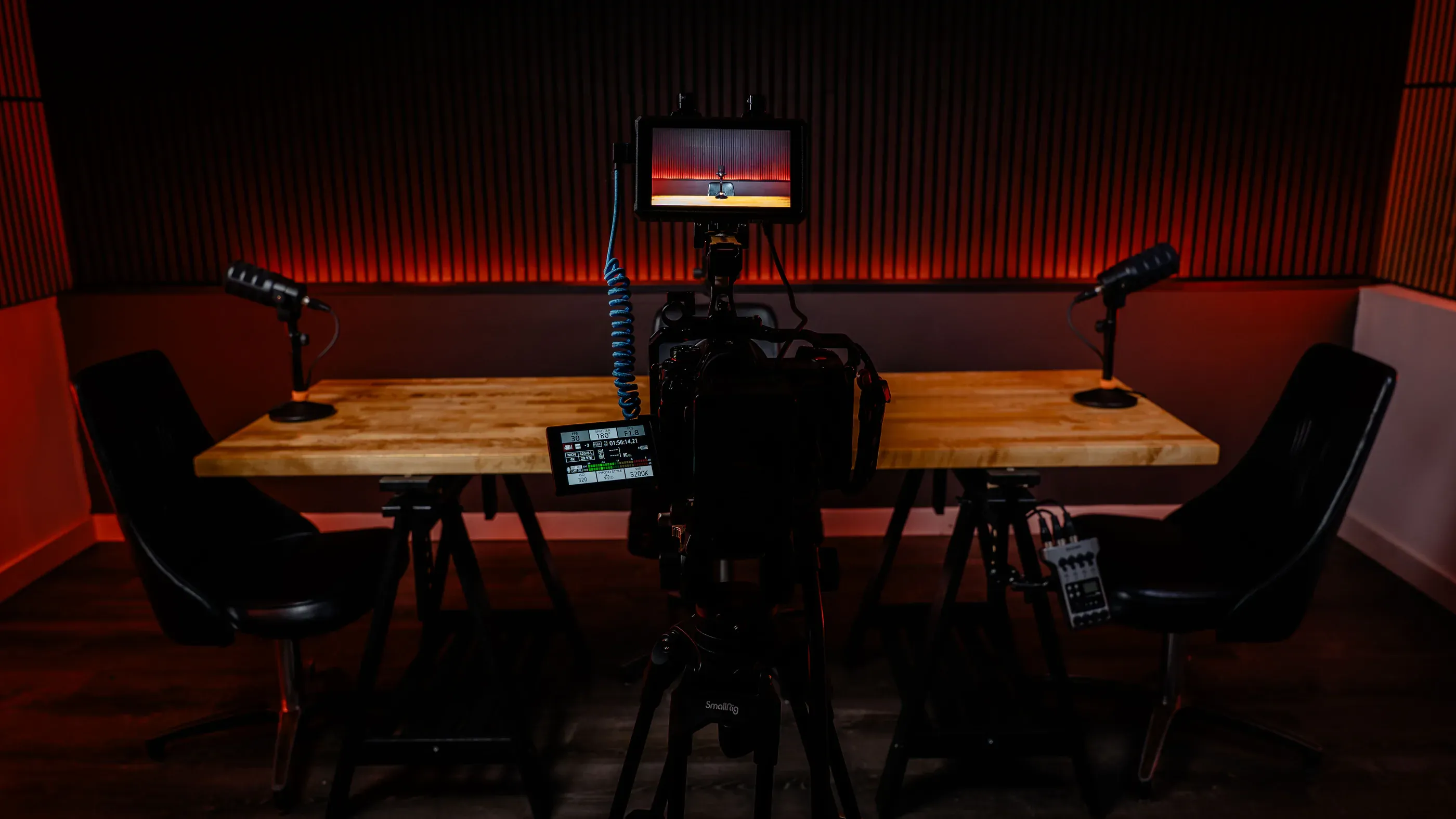 Podcast recording setup with microphones, chairs, and monitor.