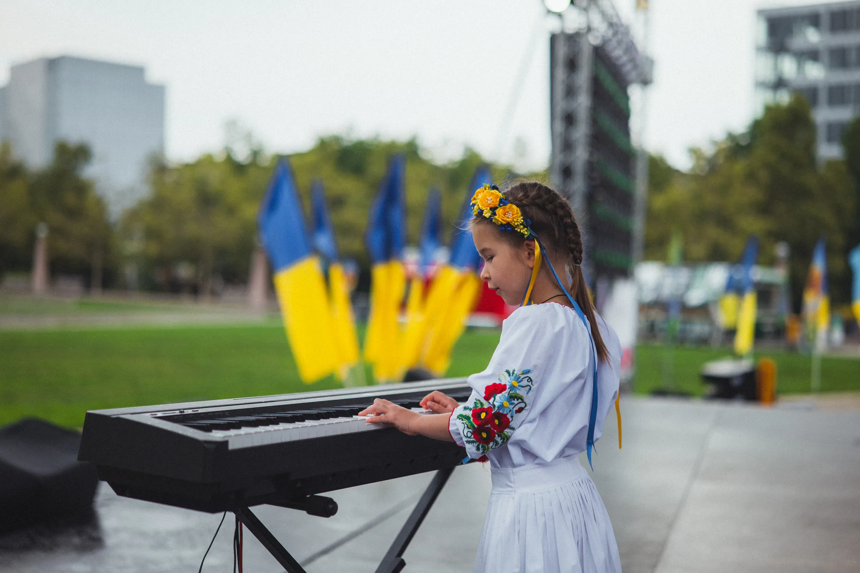 Young performer plays keyboard beside Ukrainian flags.