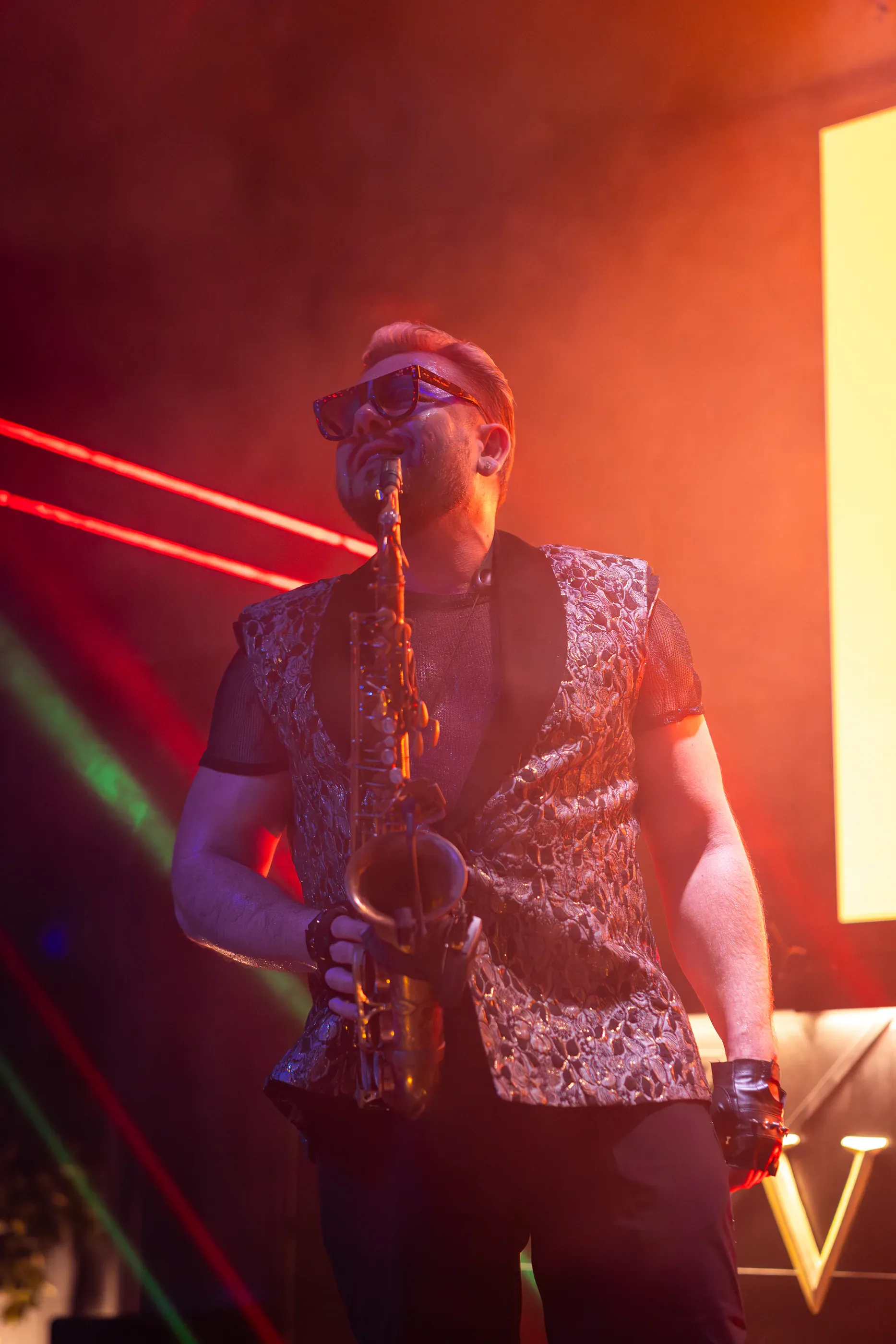 Saxophonist performs in front of orange stage light.