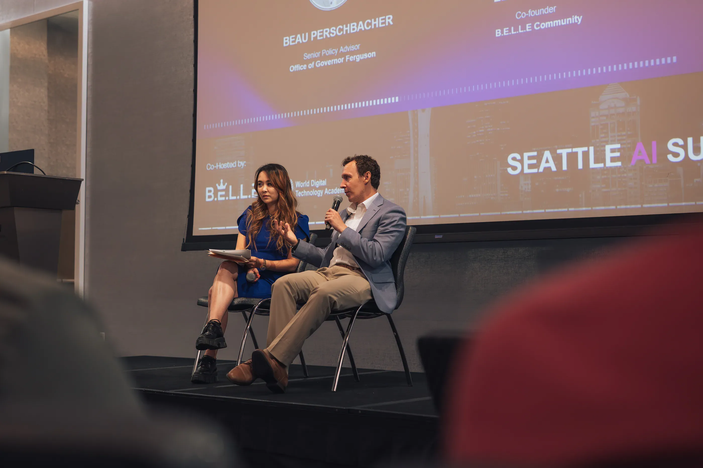 A two-person stage conversation in front of the Seattle AI Summit screen.