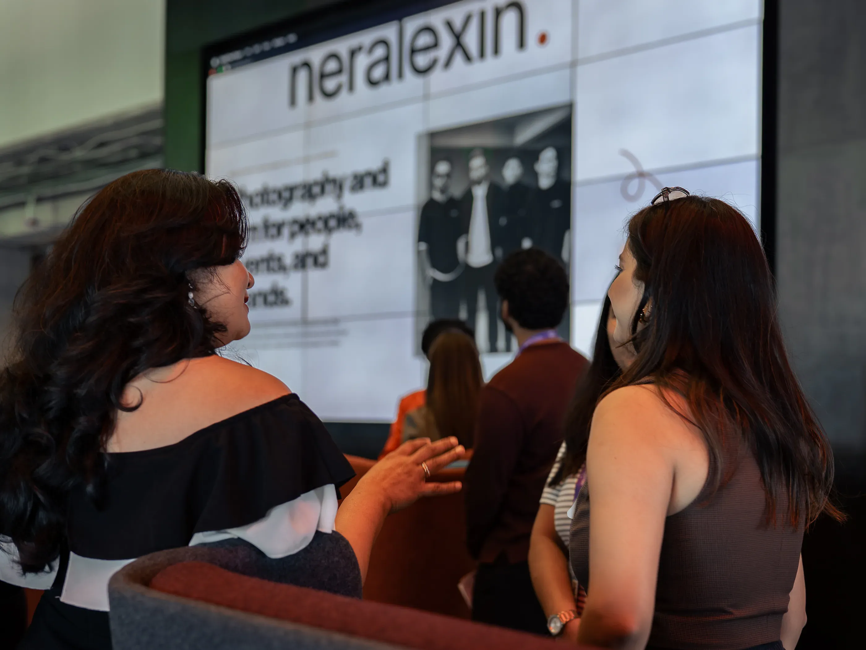 Two attendees talking in front of a partner screen showing the Neralexin wordmark.