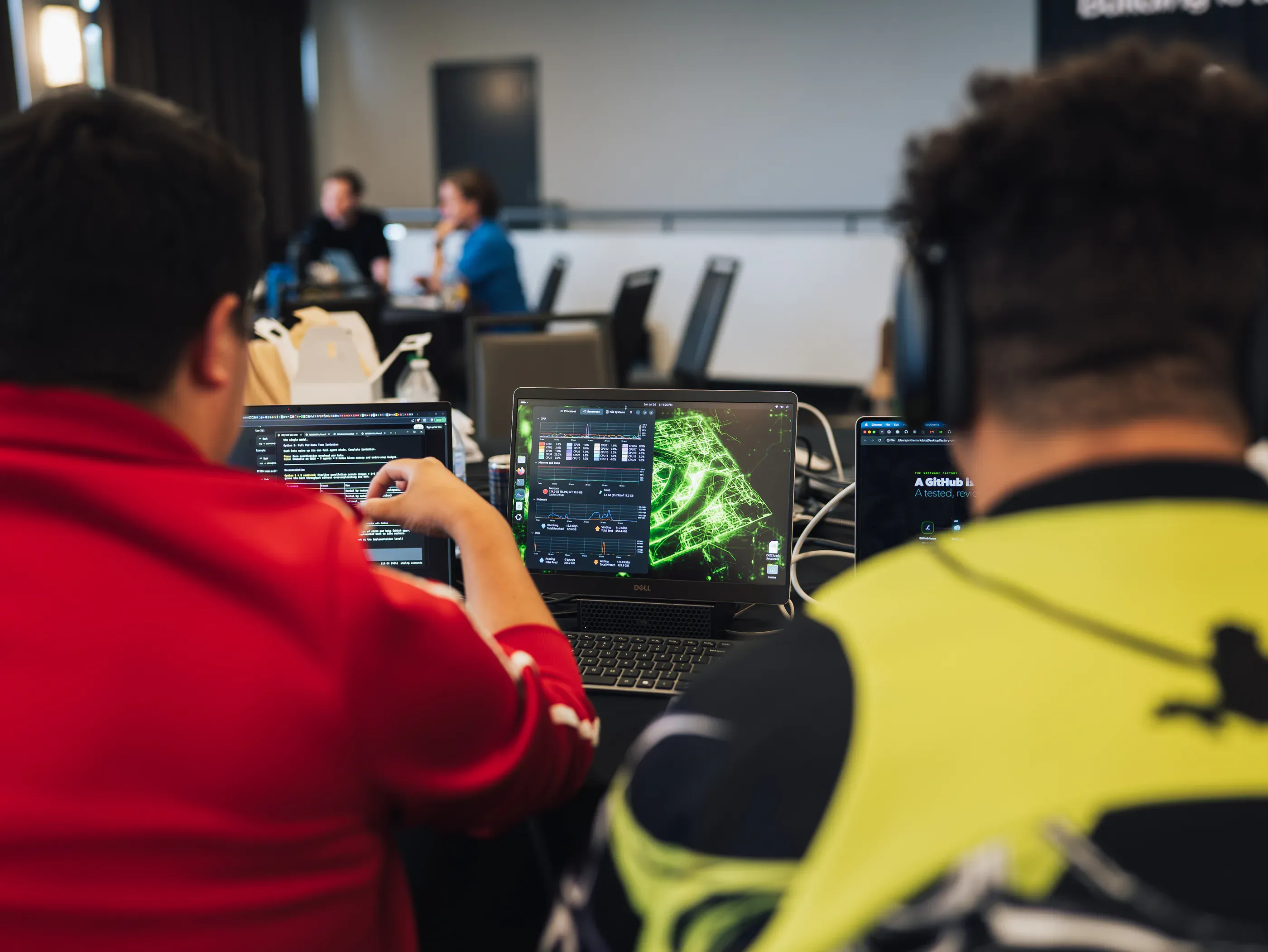 Two teammates at their laptops, one screen showing a green data visualization.
