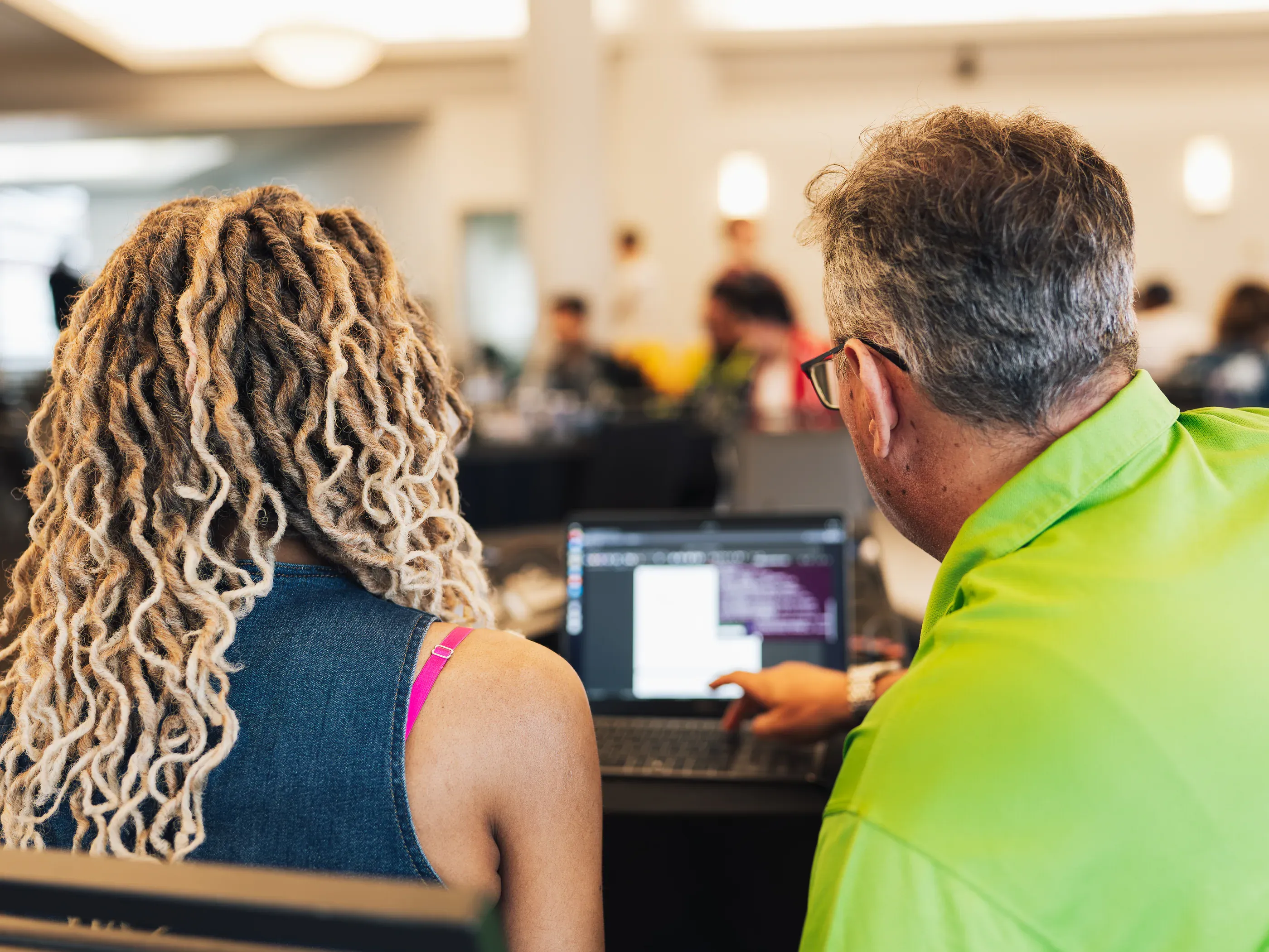 A mentor and a participant reading code together on a laptop in the main hall.