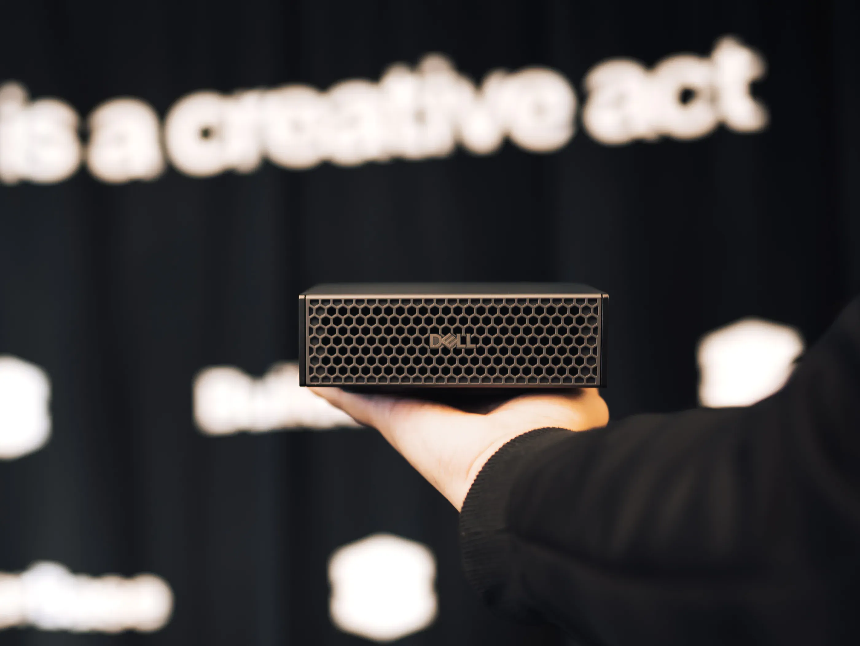 A hand holding a compact Dell workstation in front of the BuilderBase backdrop.