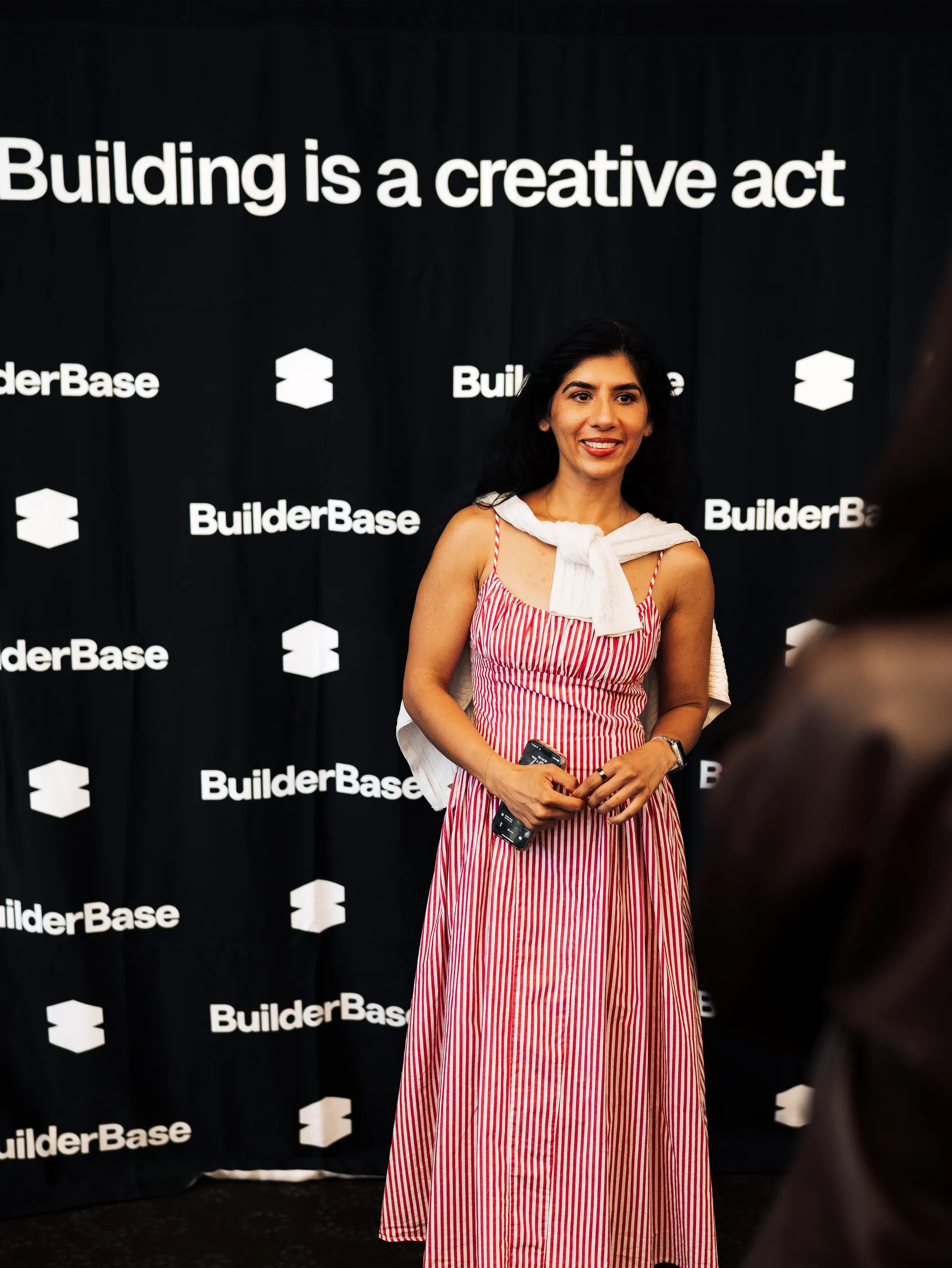 An attendee photographed at the BuilderBase backdrop reading Building is a creative act.