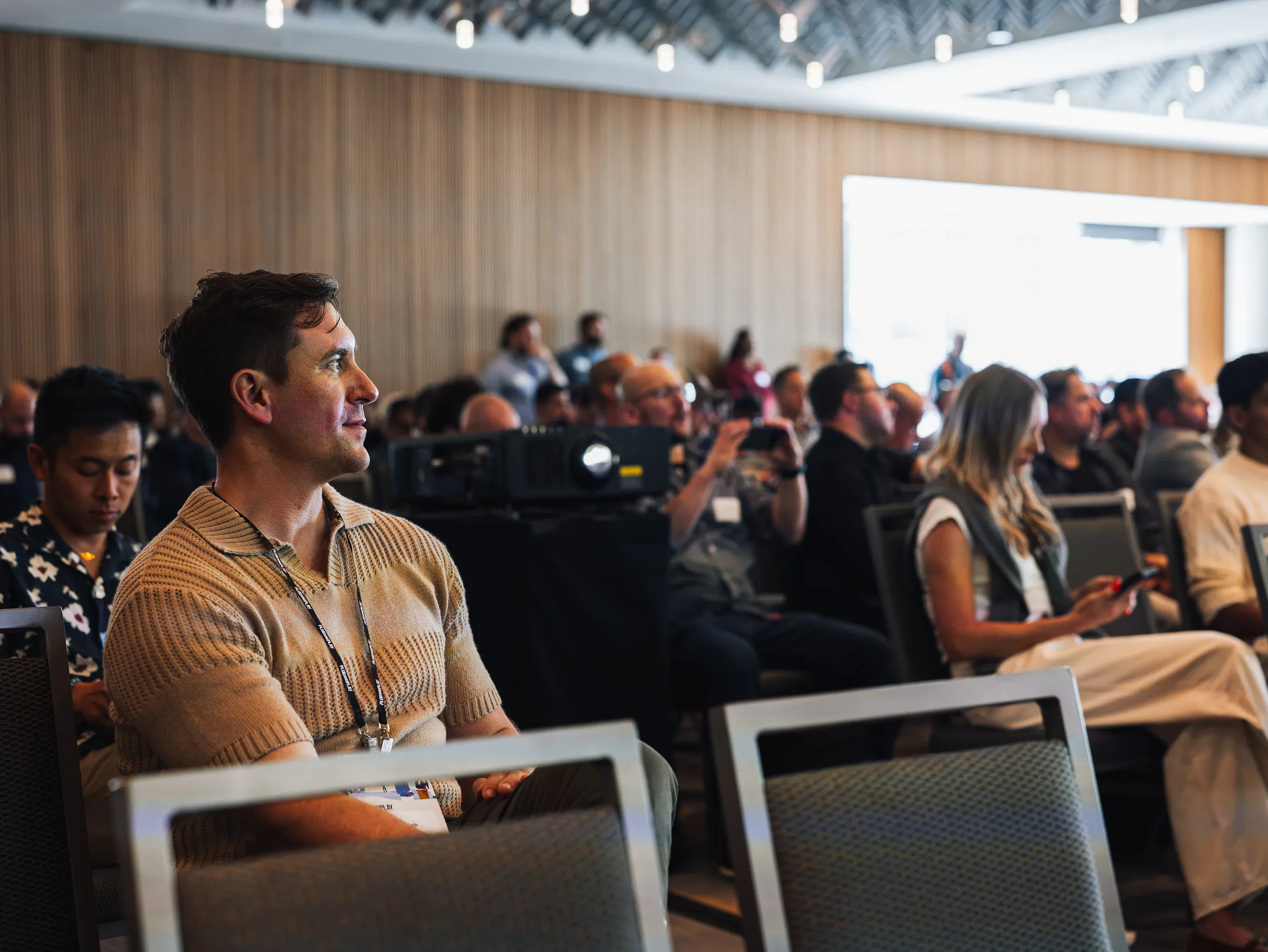Attendees watching a session in a wood-paneled conference room.