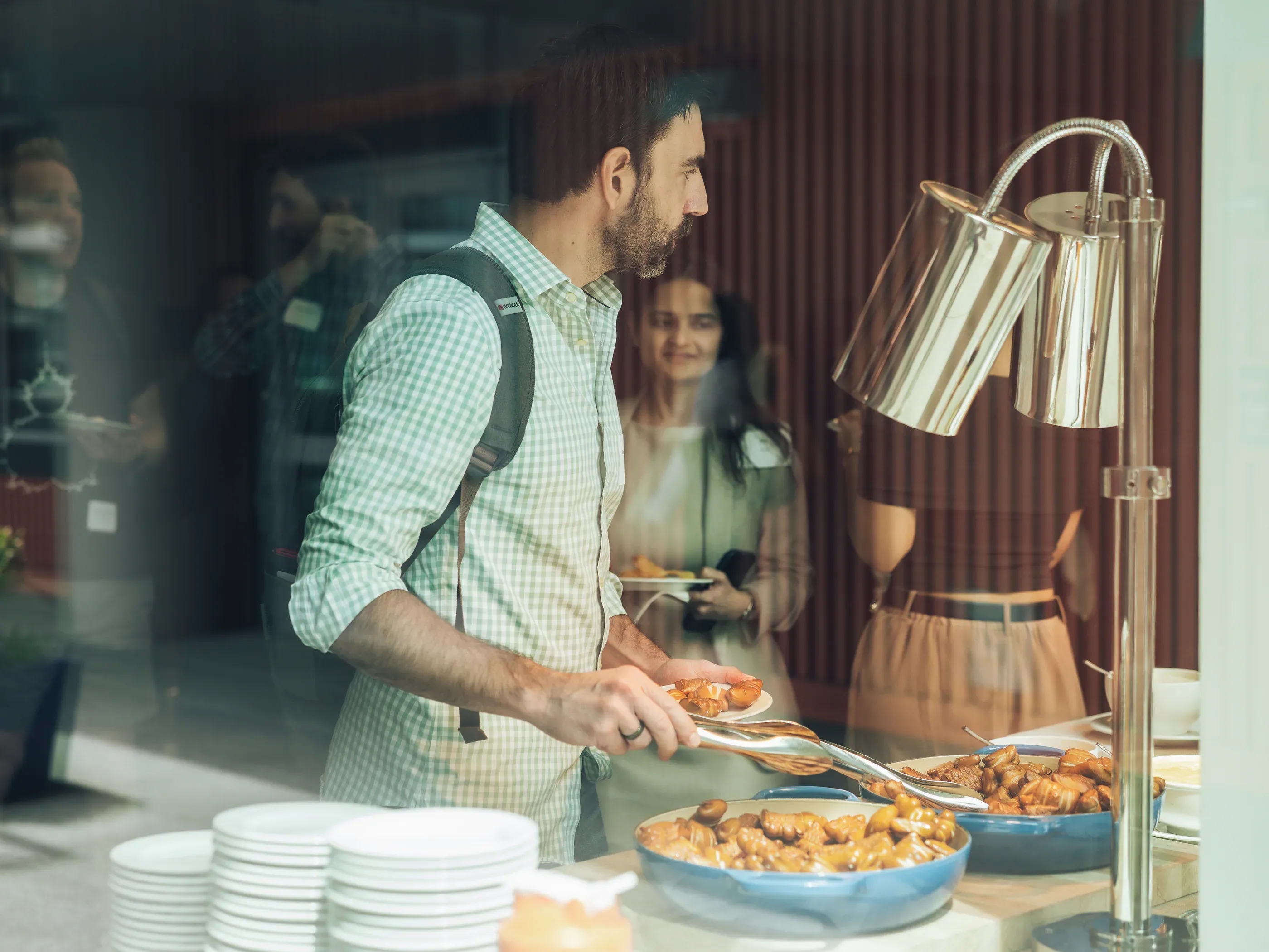 Guest serving food at the buffet during an event break, photographed through a window.