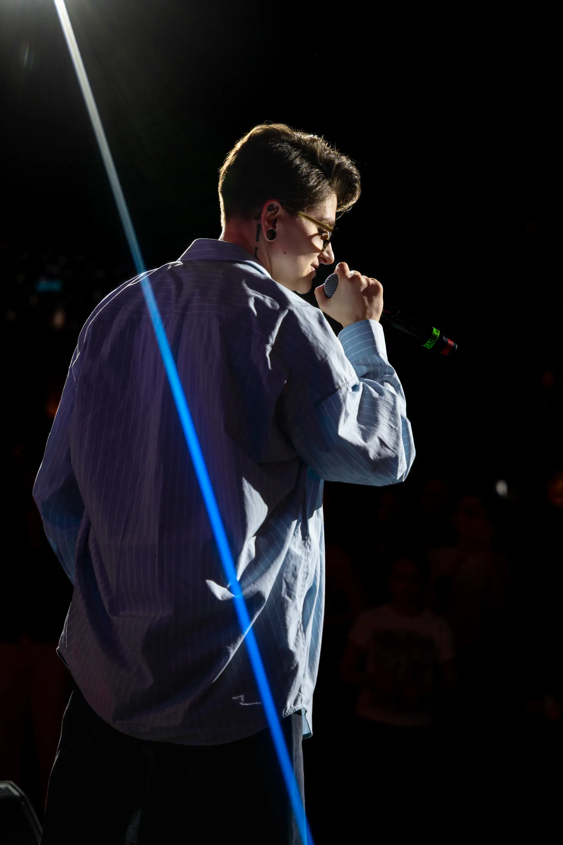 Singer performs from behind with a light flare across the frame.