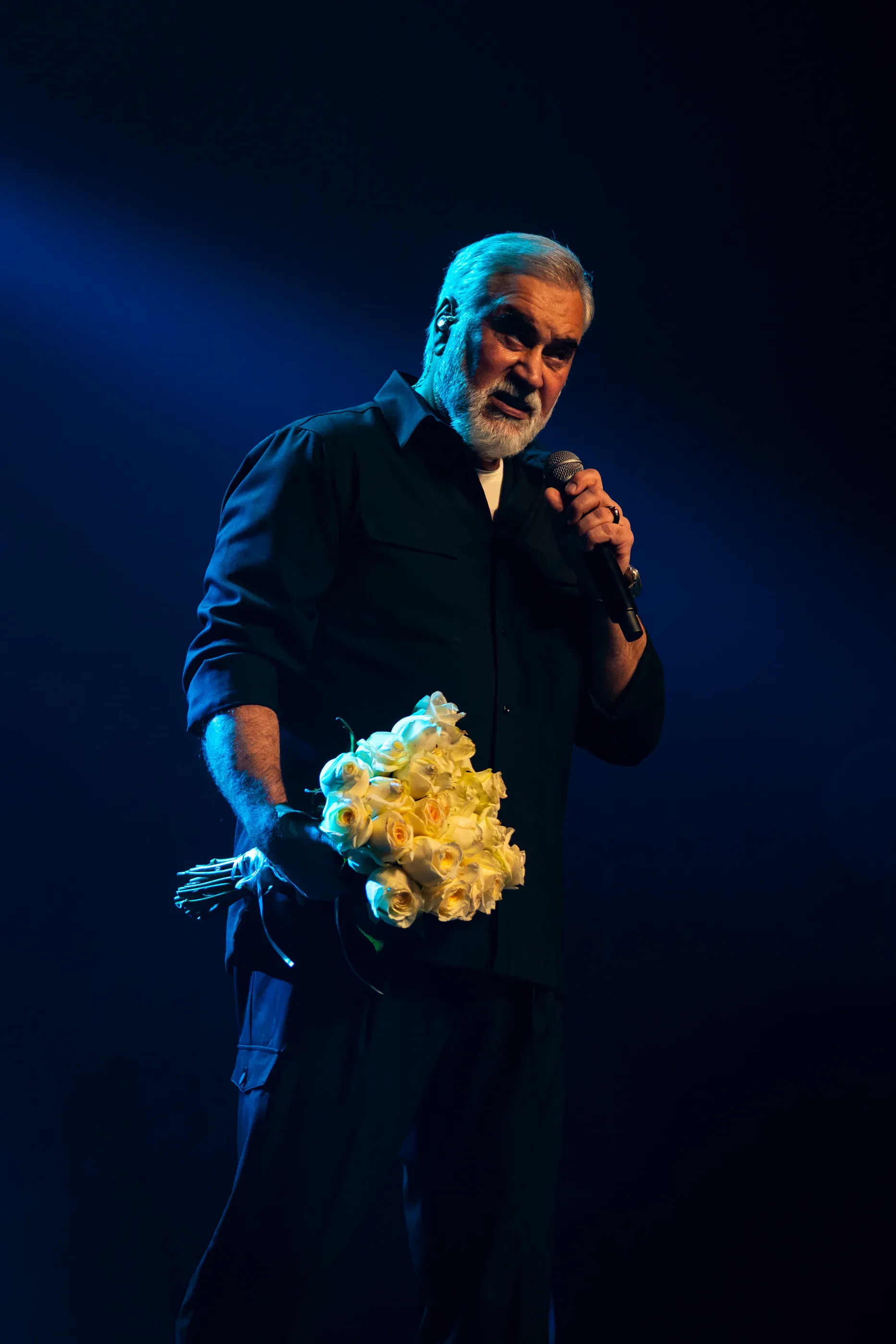 Valery Meladze holds flowers while speaking on stage.