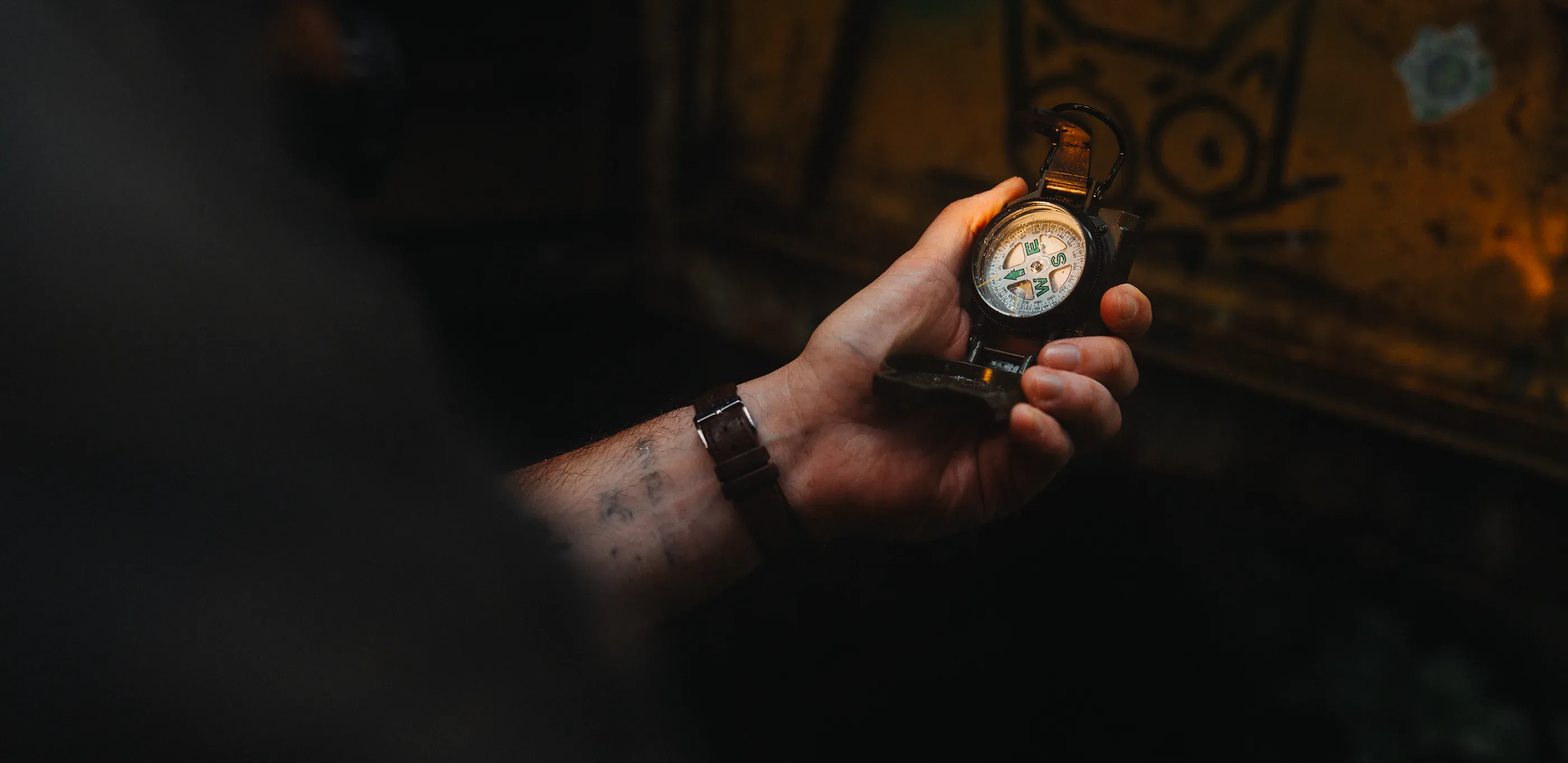 Hand holds a compass in a dark wooded setting.