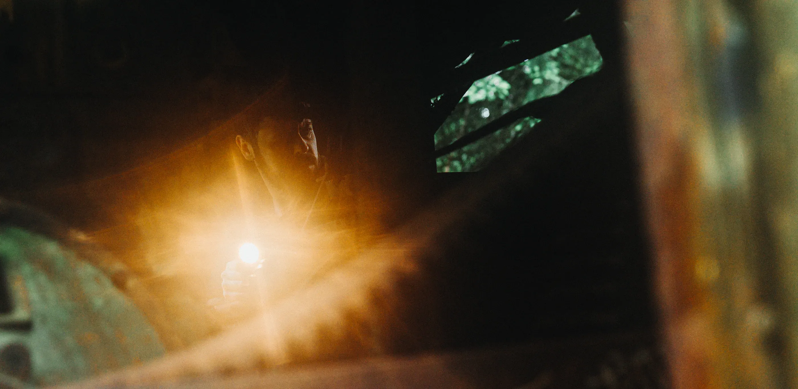 Flashlight beam cuts through rain in a forest.
