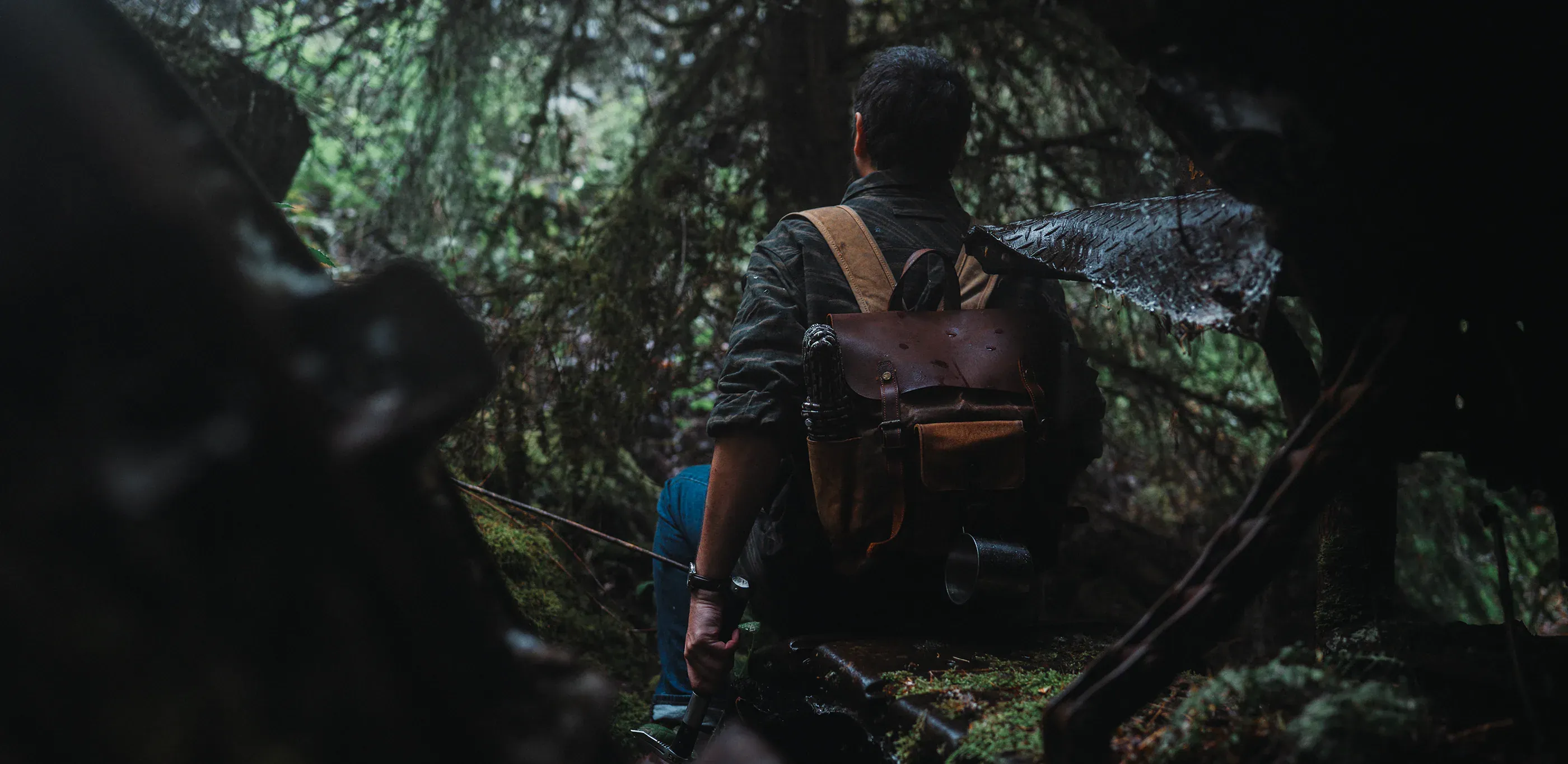 Person with backpack stands among wet mossy branches.