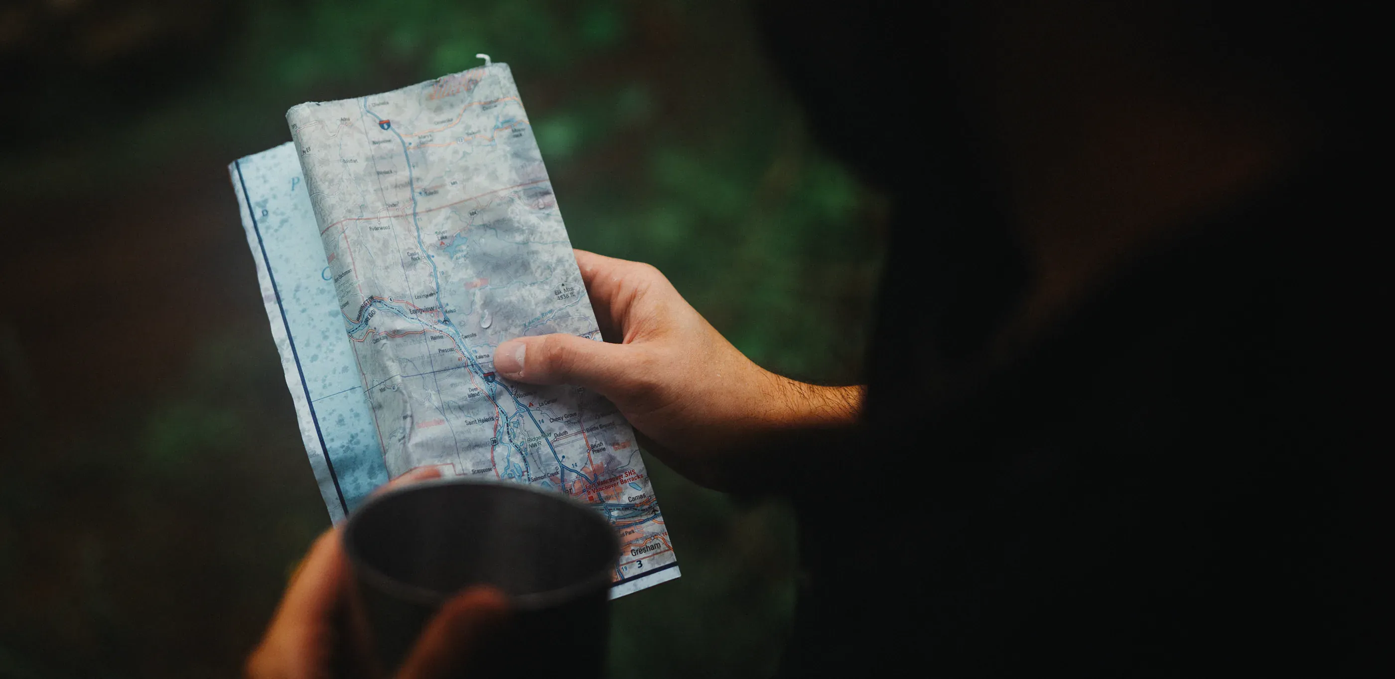 Hands hold a folded map in the forest.